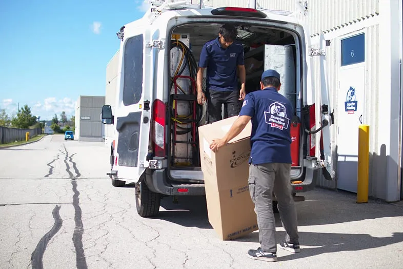 Two Superior Plumbing & Heating technicians loading equipment into a company van