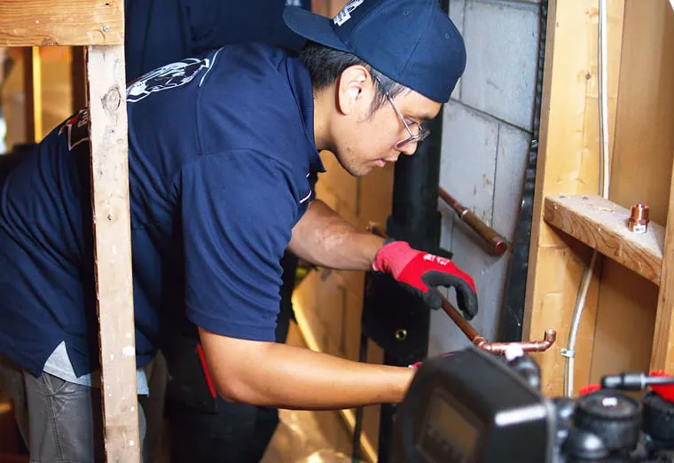 A Superior Plumbing & Heating technician working on copper pipe in an open wall