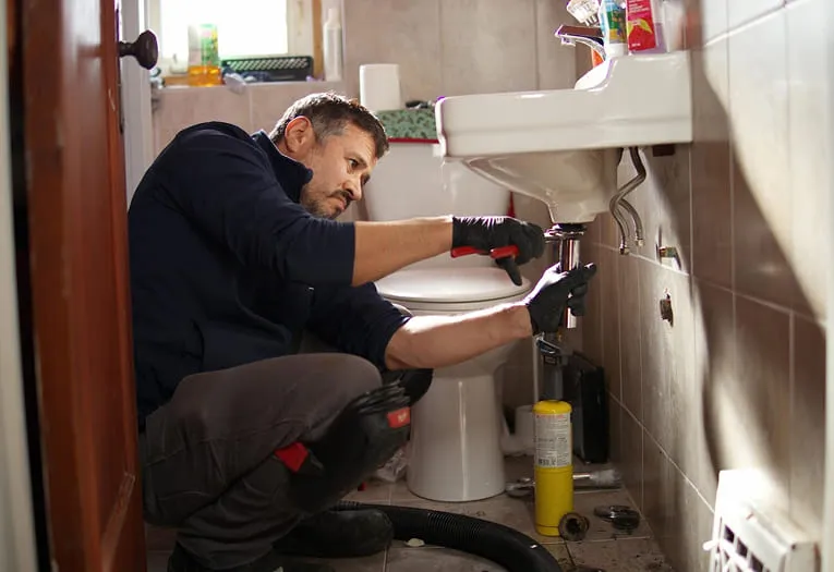 A Superior Plumbing & Heating plumber working on the pipes under a bathroom sink